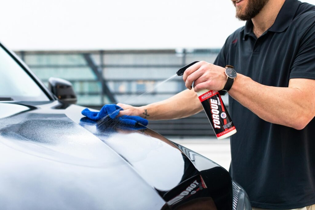 Close-up of a man cleaning a car hood with spray and microfiber cloth outdoors.